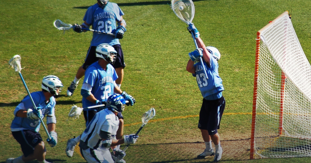 Lacrosse goalie in the crease raising the goalie stick to make a save, defenders in front of the net